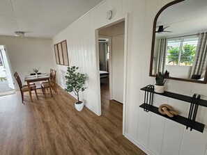 Ein Zimmer mit einem Esstisch, Stühlen, einer Topfpflanze, einem Spiegel und einem Regal mit Pflanze und Dekorationsobjekt.