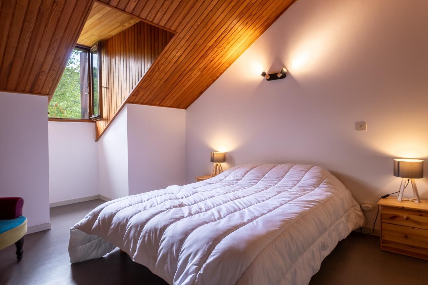 A bedroom with a sloped ceiling, a large bed, two bedside lamps, and a window.