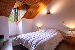 Une chambre avec un plafond en pente, un grand lit, deux lampes de chevet et une fenêtre.