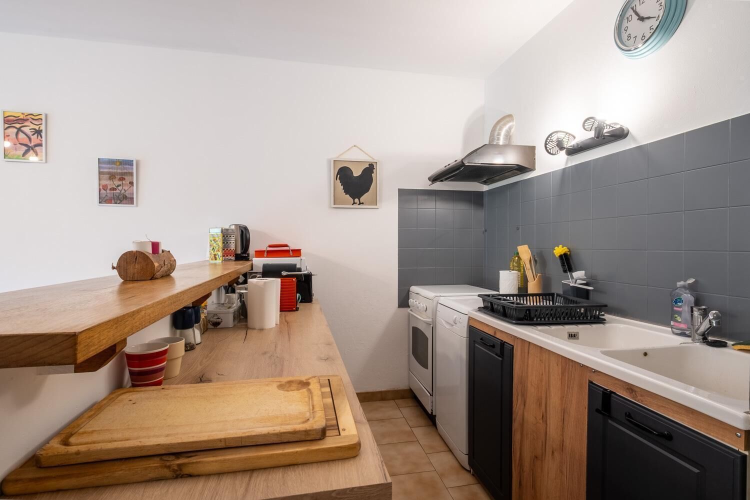 A modern kitchen with a wooden countertop, a built-in oven, a dishwasher, and a wall-mounted clock.