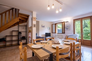 Un coin repas avec une table et des chaises en bois, un escalier, une bibliothèque et une vue sur la verdure par une fenêtre.