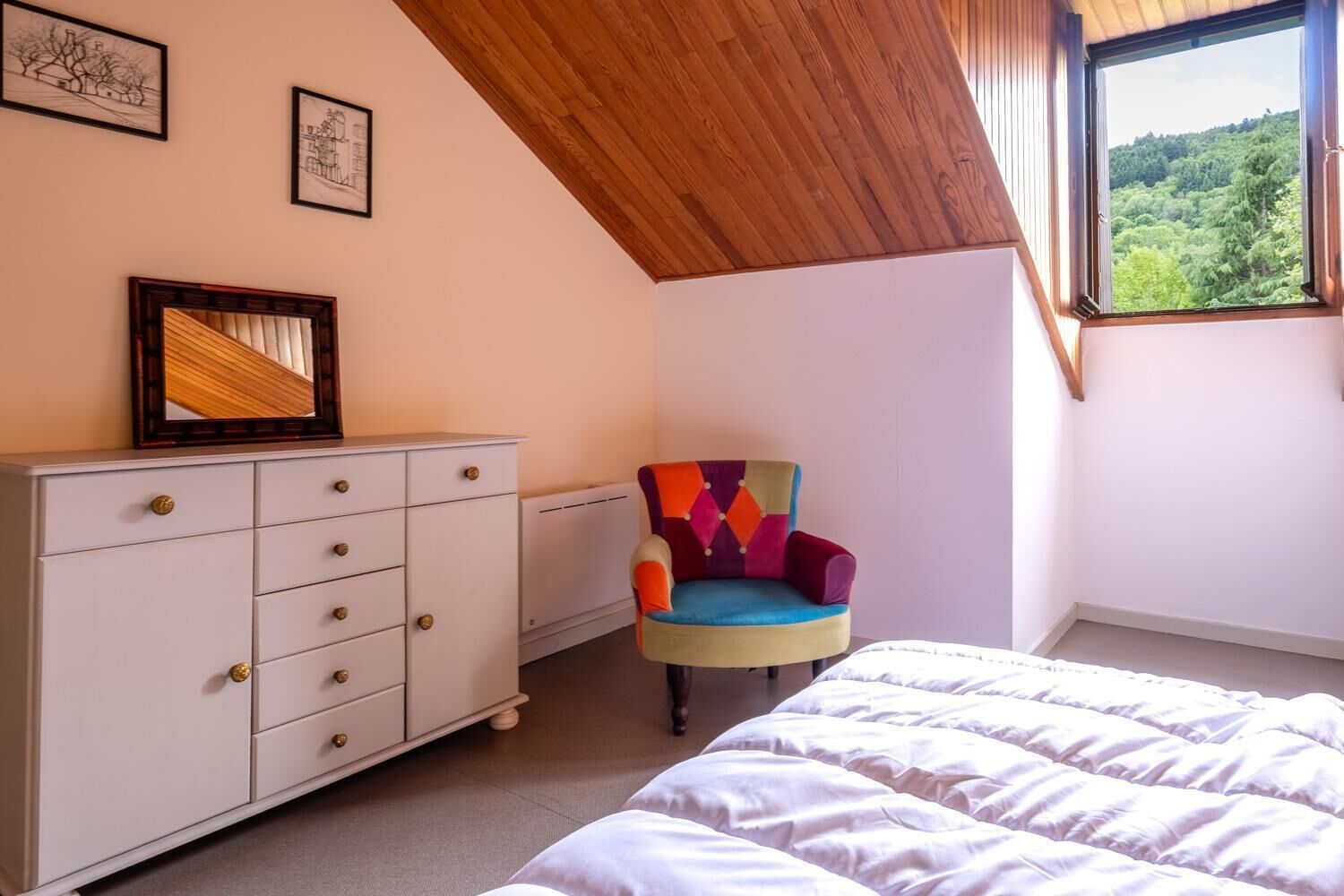 A bedroom with a bed, a dresser, a chair, and a window with a view of trees.