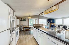 A modern kitchen with white cabinetry, a wooden dining table, and a black countertop. - The Lake House – Lake Champlain Waterfront Retreat (Colchester)
