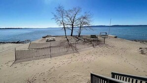 Ein Sandstrand mit einer Holzlattenumrandung, einer Bank und einem Baum.