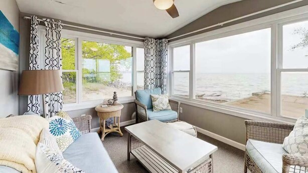 Ein Wintergarten mit Blick auf den Strand, ein Deckenventilator und Korbmöbel.