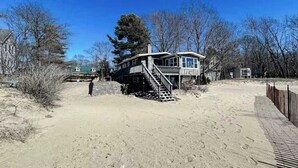 Ein Strandhaus mit einer Treppe, die zum Haupteingang führt, umgeben von Bäumen und einem Sandstrand.