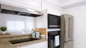 Eine moderne Küche mit weißen Schränken, einer Granitarbeitsplatte, einem Edelstahlkühlschrank und einem schwarzen Backofen.