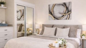 Ein Schlafzimmer mit einem großen Bett, einem Nachttisch, einem Spiegel und einem an der Wand hängenden abstrakten Gemälde.