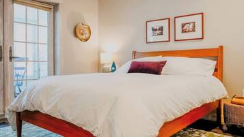 A hotel room with a bed, a nightstand, a lamp, two framed pictures on the wall, and a door leading to an outdoor area.