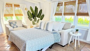 Una habitación luminosa con una cama, dos sofás, una mesita y una planta grande.
