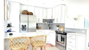 Una cocina moderna con armarios blancos, un refrigerador de acero inoxidable, una estufa negra y dos taburetes de mimbre.