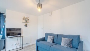 Un soggiorno moderno con un divano blu, una TV a schermo piatto su un mobile, un elemento decorativo a parete e una lampada a soffitto.