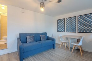 Un salon moderne avec un canapé bleu, deux fauteuils blancs, une table à manger en bois et trois panneaux décoratifs muraux.
