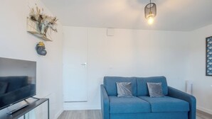 Un soggiorno moderno con un divano blu, una televisione a schermo piatto su un tavolino in vetro e un elemento decorativo a parete.
