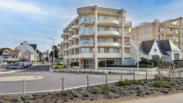 Un edificio residencial de varios pisos con balcones, una glorieta y una calle con automóviles estacionados.