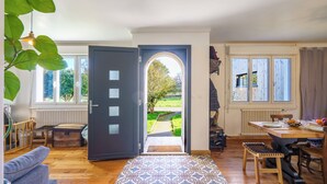 Ein Zimmer mit Holzboden, einem gemusterten Teppich, einem für zwei Personen gedeckten Esstisch und Blick durch eine offene Tür auf einen Garten.