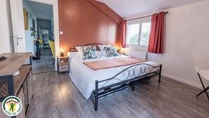 Ein Schlafzimmer mit Bett, Nachttischen, einem fensterbelaubten Fenster, Holzboden und Blick auf einen Flur.