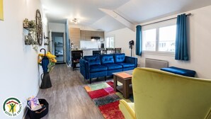 Eine moderne Wohnung mit einem blauen Sofa, einem gelben Sessel und einer Küche im Hintergrund.
