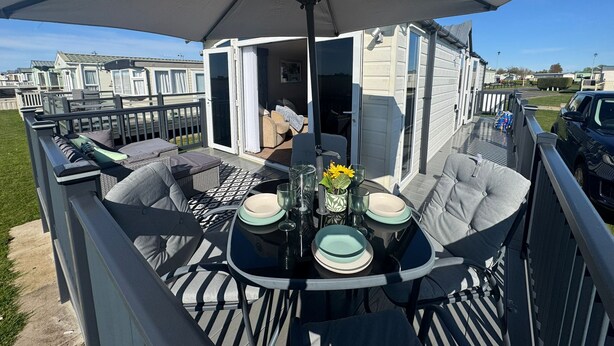 Un espacio al aire libre techado con una mesa dispuesta para dos personas, un sofá y un ventanal corredero que da a una habitación.