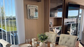 Un comedor con una mesa de madera, sillas tapizadas, un jarrón con follaje y un televisor montado en la pared.