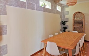 Een eethoek met een houten tafel en witte stoelen, een mandenplank en een potplant.