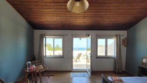 Ein Zimmer mit Holzboden, einem Bett, einem Fernseher, einem Tisch mit Stühlen und großen Fenstern mit Vorhängen.