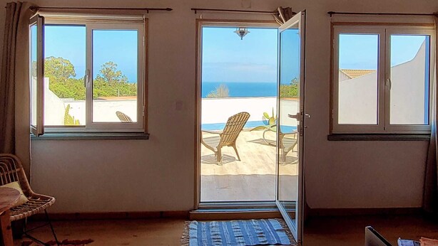 Ein Zimmer mit Holzboden, zwei Schiebegläser zu einer Terrasse im Freien mit Blick aufs Meer.