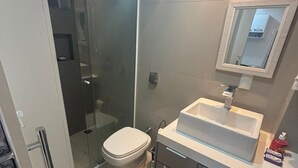 Une salle de bain moderne avec une douche à parois de verre, des toilettes blanches et un lavabo blanc avec un miroir au-dessus.