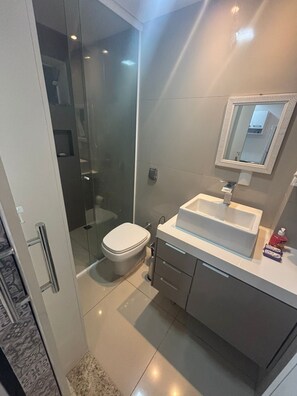 Une salle de bain moderne avec une douche à parois de verre, des toilettes blanches et un lavabo blanc avec un miroir au-dessus.