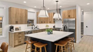 Una cocina moderna con armarios de madera, una isla grande con taburetes, electrodomésticos de acero inoxidable e iluminación colgante.