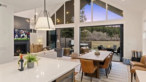 Una sala de estar moderna con una gran mesa de comedor, asientos cómodos, una chimenea y vistas al exterior.
