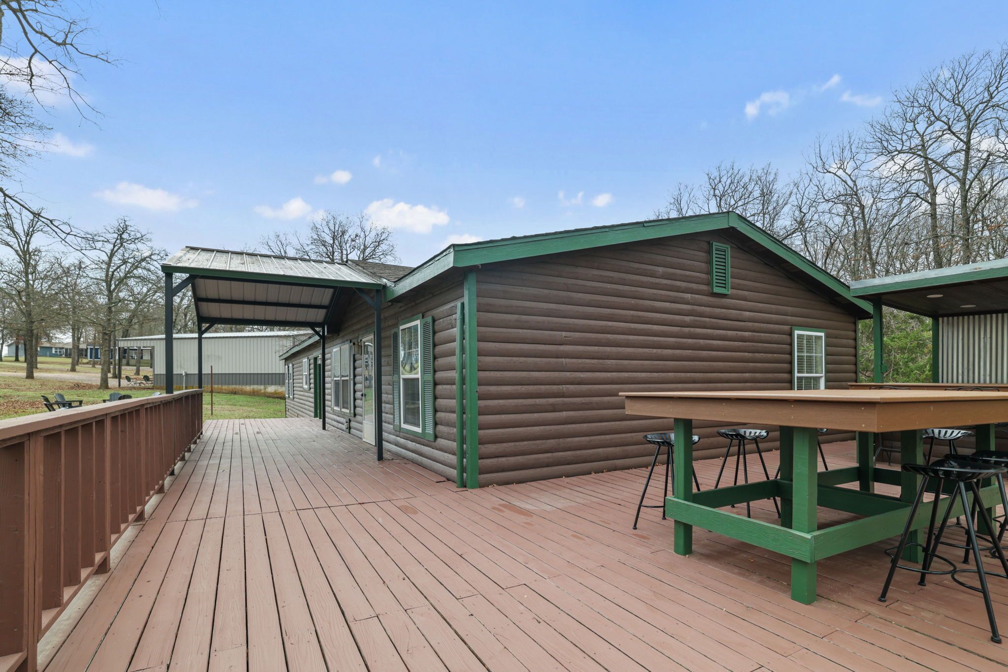 A wooden deck with a table and chairs, a covered area, and a log cabin-style building.