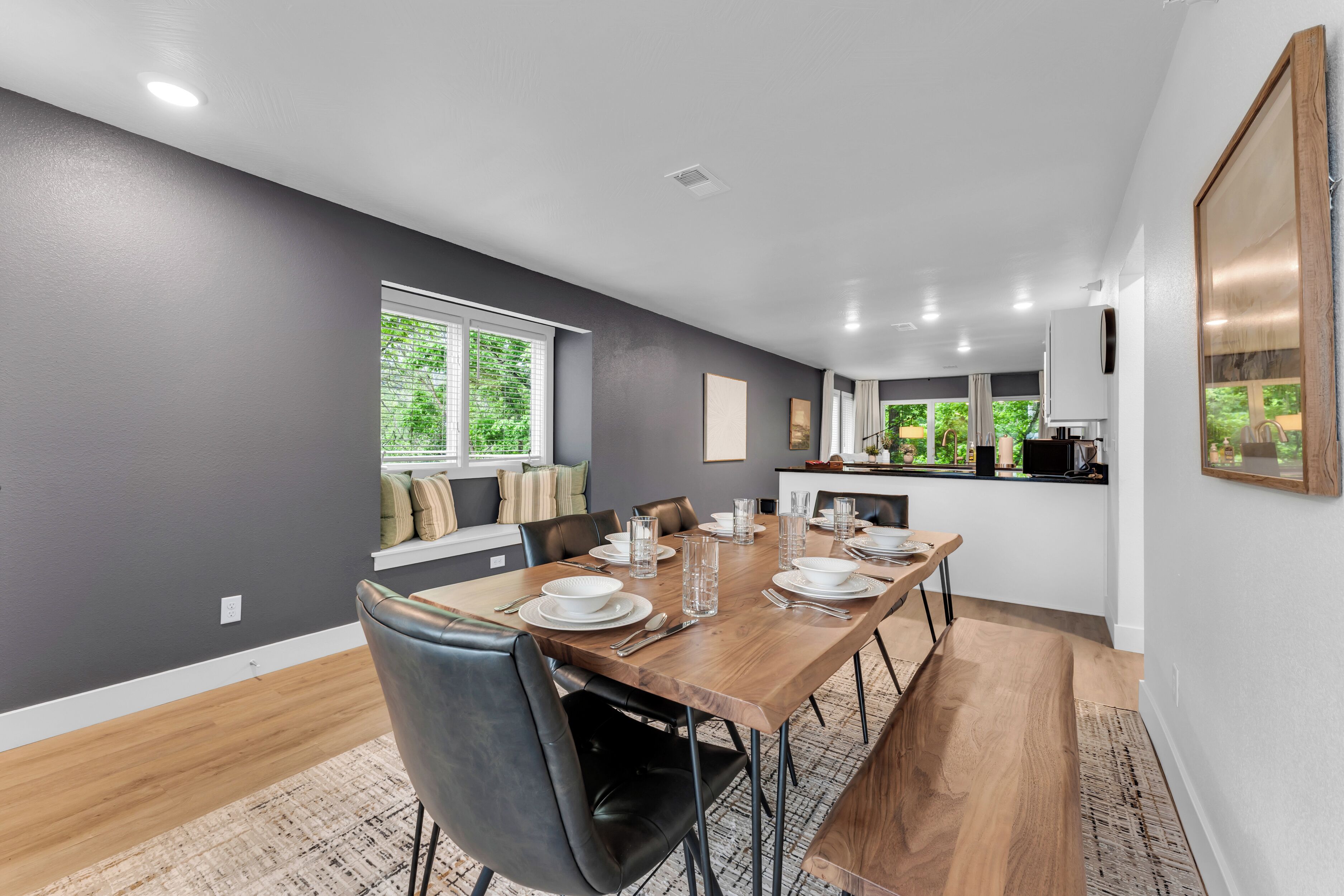 A modern dining area with a wooden table set for six, surrounded by black leather chairs.