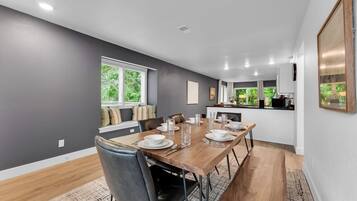 A modern dining area with a wooden table set for six, surrounded by black leather chairs.