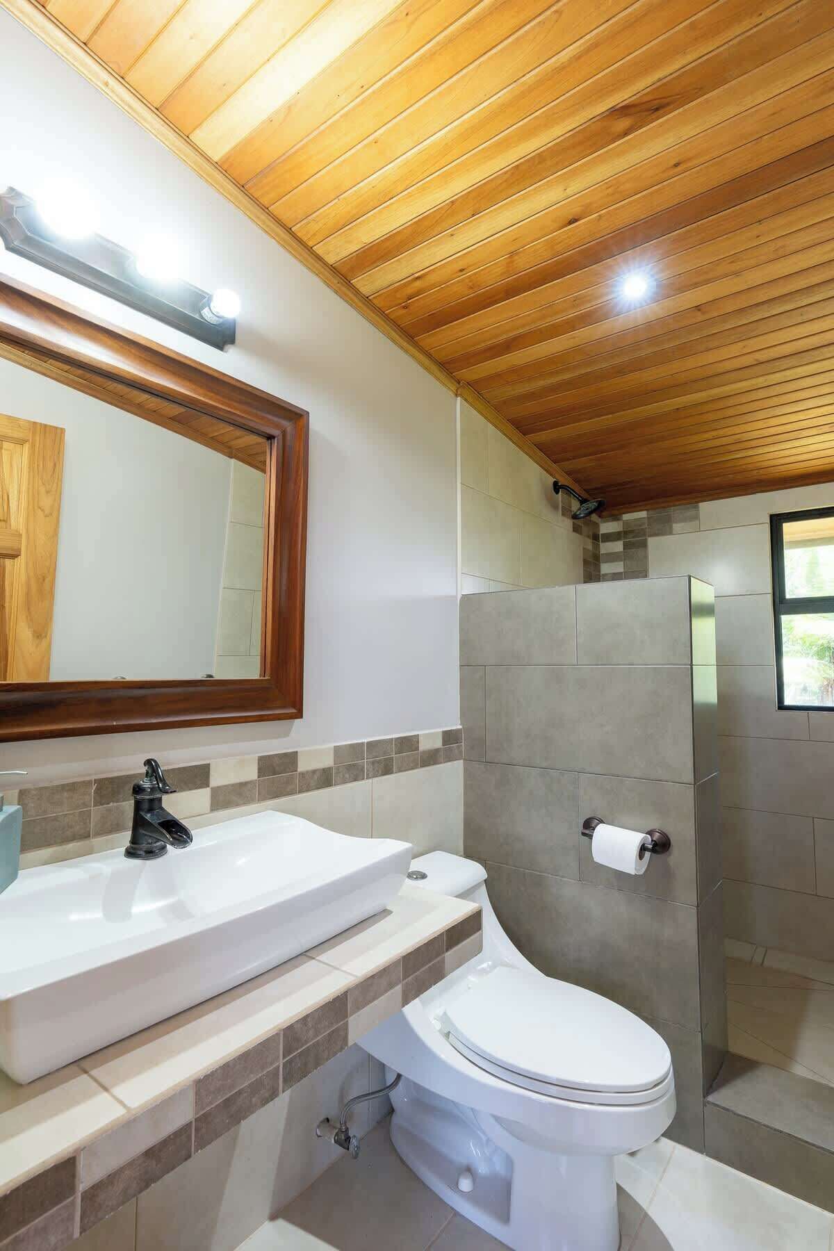 Ein Badezimmer mit Holzboden, einem weißen Waschbecken, einer Toilette und einer Duschkabine.