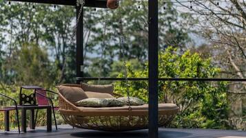 Un espace aménagé au bord de la piscine, comprenant un fauteuil suspendu, une table et une pergola illuminée de guirlandes lumineuses.