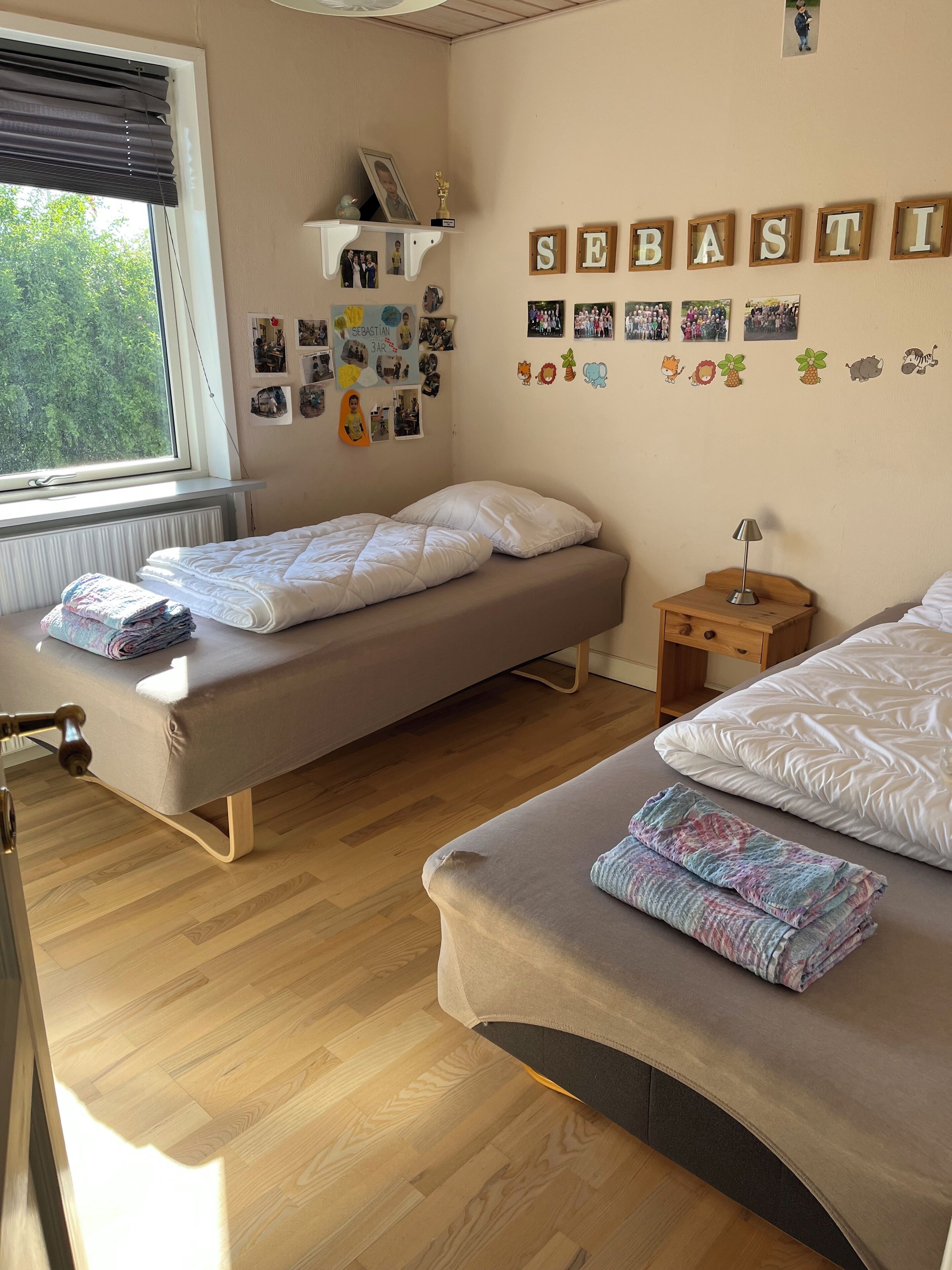 A bedroom with two single beds, a shelf with photos, and a wall with alphabet letters.
