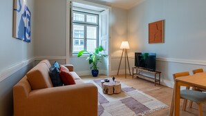A living room with a sofa, a coffee table, a TV, a dining table, and a potted plant. - FLH Heart of Rossio Flat III (Lisboa ciudad)