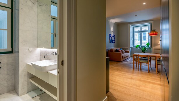 A modern bathroom with a white sink and mirror, a wooden dining table with chairs, a sofa, and a large window with a view. - FLH Heart of Rossio Flat III (Lisboa ciudad)