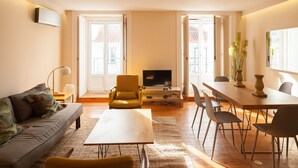 A living room with a sofa, a coffee table, a TV, and a dining area with chairs and a table. - FLH Downtown City Elegance Apartment (Lisboa ciudad)