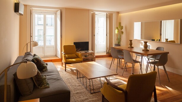 A modern living room with a sofa, coffee table, yellow armchair, and dining table with chairs. - FLH Downtown City Elegance Apartment (Lisboa ciudad)