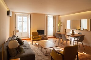 A modern living room with a sofa, coffee table, yellow armchair, and dining table with chairs. - FLH Downtown City Elegance Apartment (Lisboa ciudad)