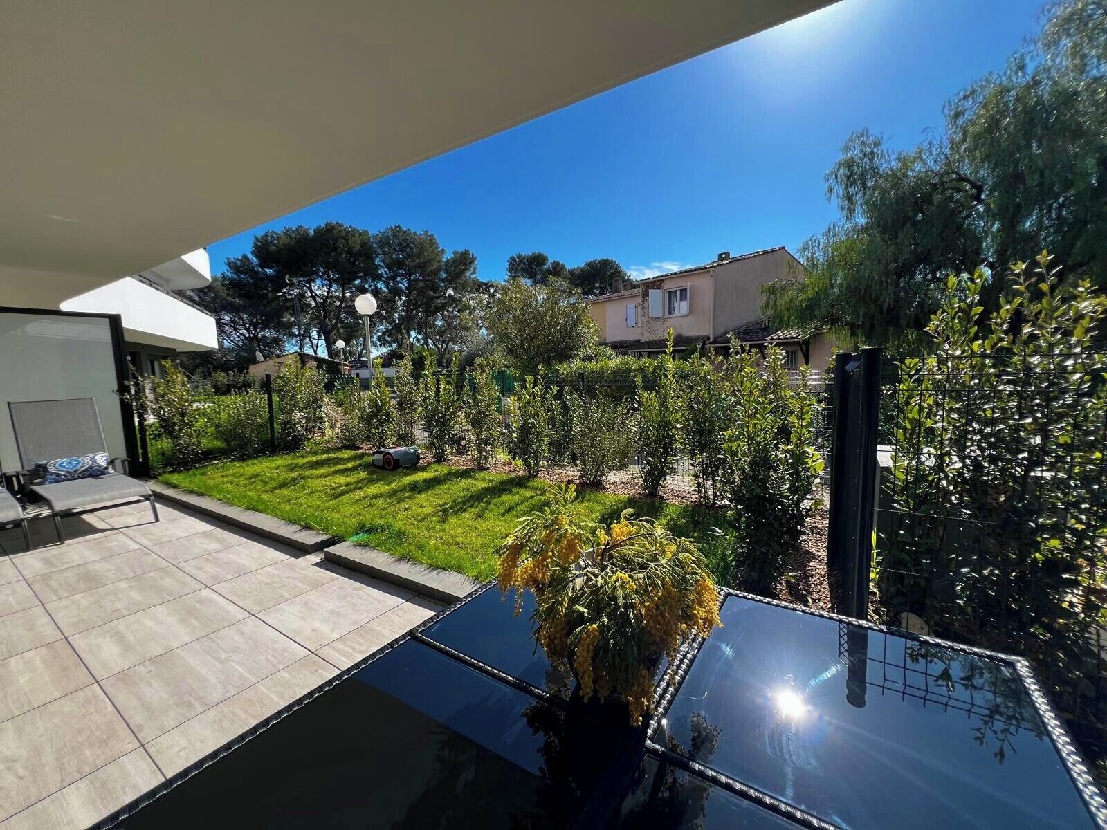 Une terrasse extérieure moderne, dotée d’une table en verre, d’un petit coin salon et d’une pelouse bien entretenue.