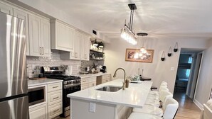 A modern kitchen with white cabinetry, stainless steel appliances, and a central island with bar stools.