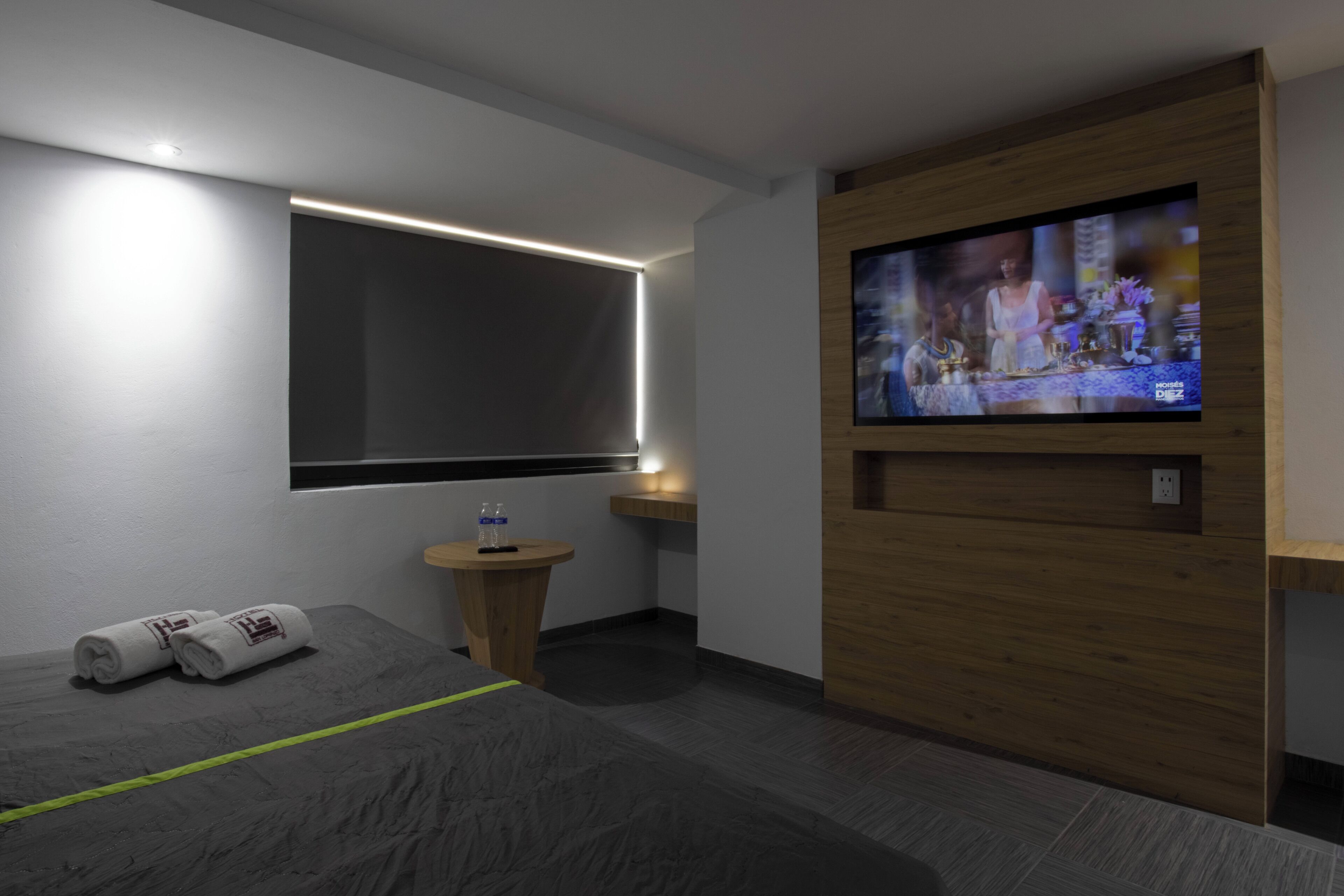 A modern hotel room with a bed, a TV, a small table, and a window.