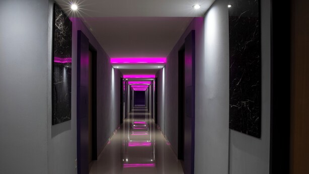 A modern hallway with reflective flooring, a central light source, and a series of doors on either side.