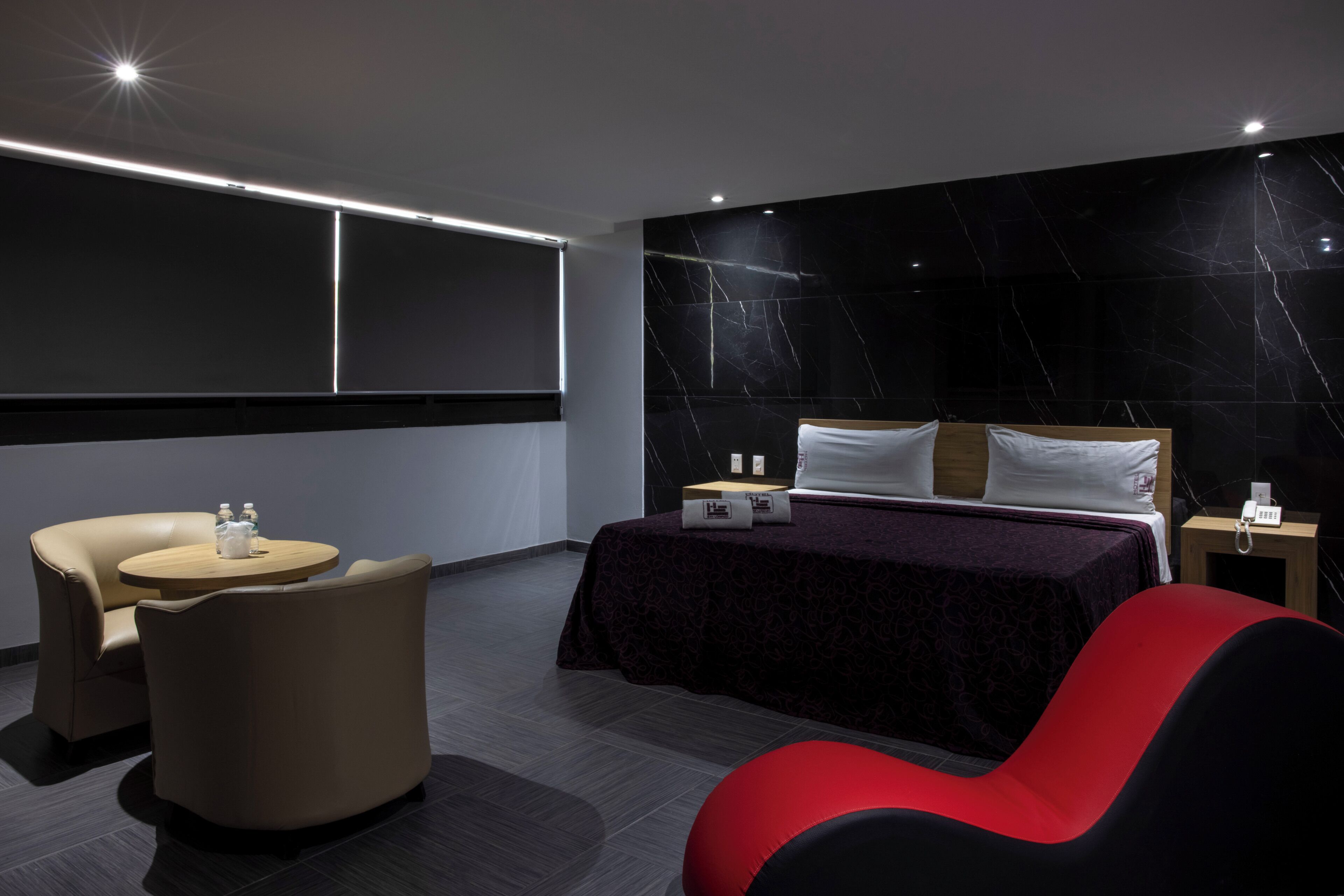 Una habitación de hotel moderna con una cama, una mesa redonda, dos sillas y un ventanal grande.