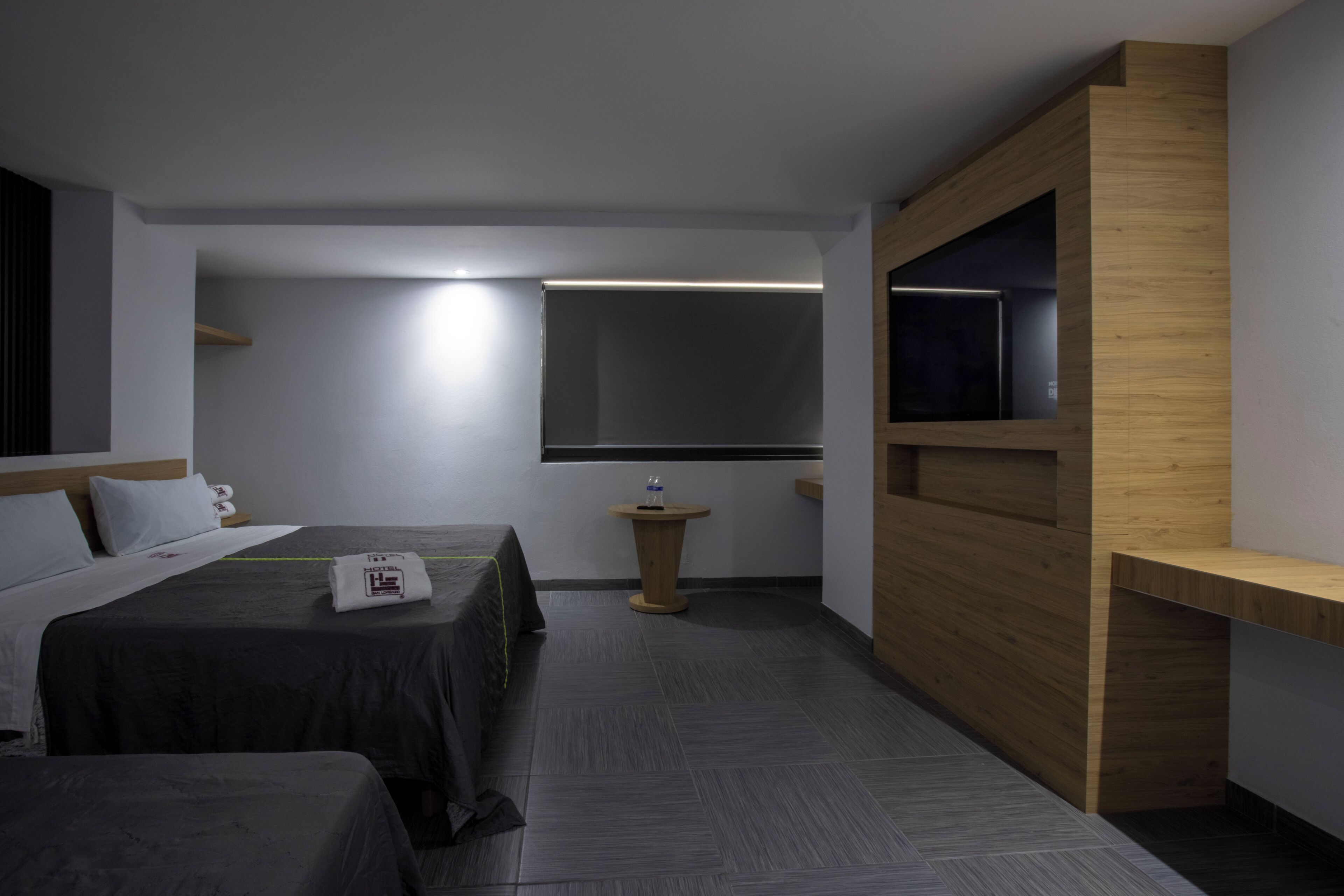 A hotel room with a bed, bedside table, and a built-in TV shelf.