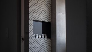 A modern bathroom with a geometric patterned wall, a white toilet, and a small shelf with toiletries.