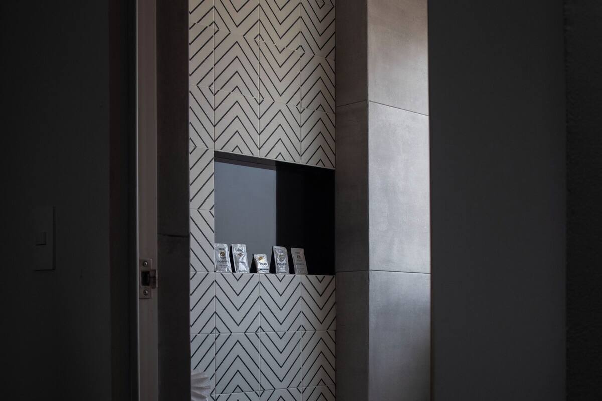 Een moderne badkamer met een wand met een geometrisch patroon, een wit toilet en een klein plankje met toiletartikelen.